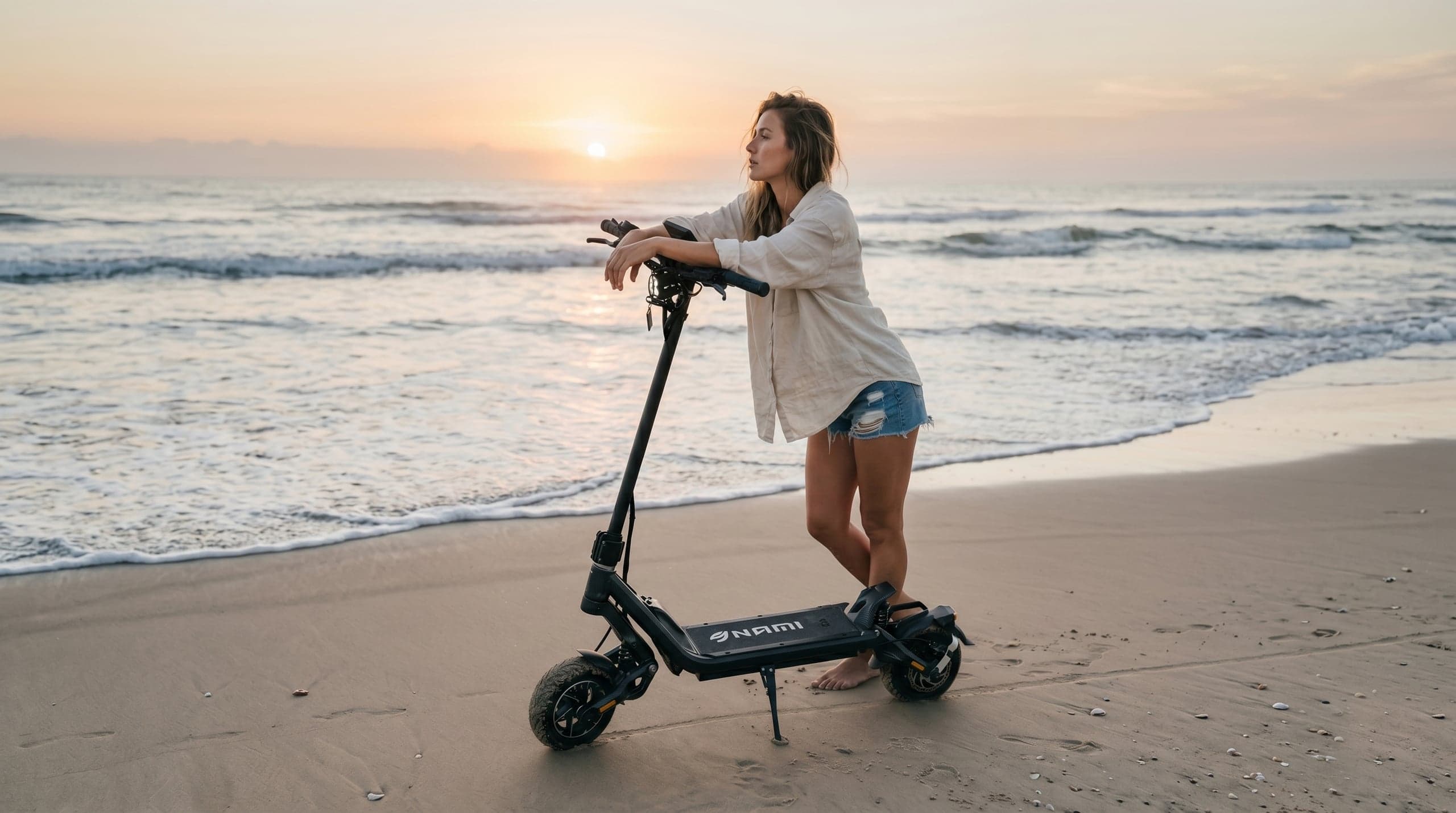 Rider leaning on a Nami Klima electric scooter at the shoreline at sunrise