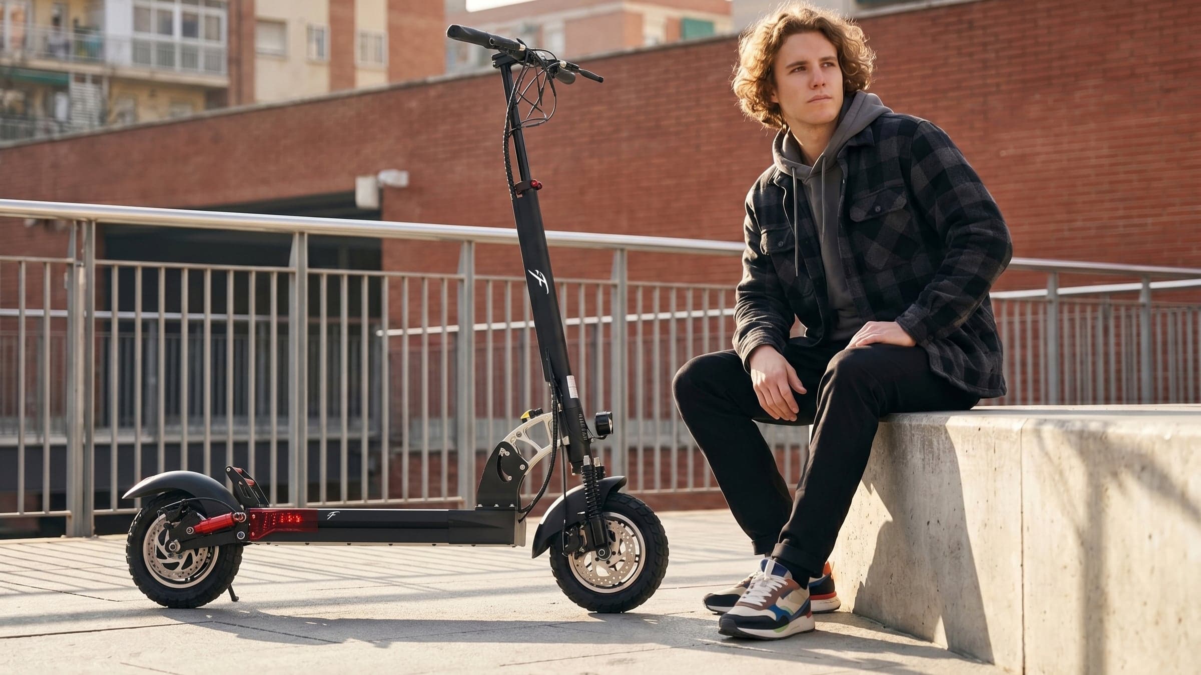 F1 Scooters rider resting on a concrete bench next to a folding commuter scooter in a sunlit urban neighborhood